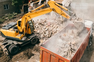 Excavator breaks building and loads construction waste into truck with its bucket. Demolition of building.