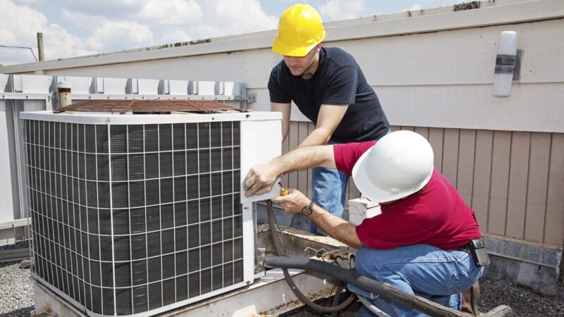 Two professional contractors working on an air conditioning unit on a rooftop