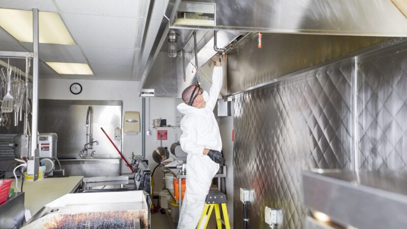A Commercial kitchen worker washing up at sink in professional clothes