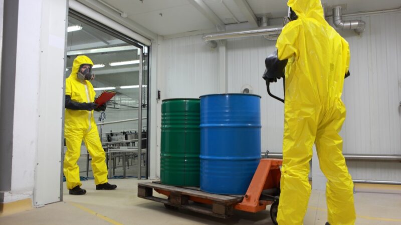 Two specialists in protective uniforms,masks,gloves and boots transport barrels of chemicals on forklift in factory