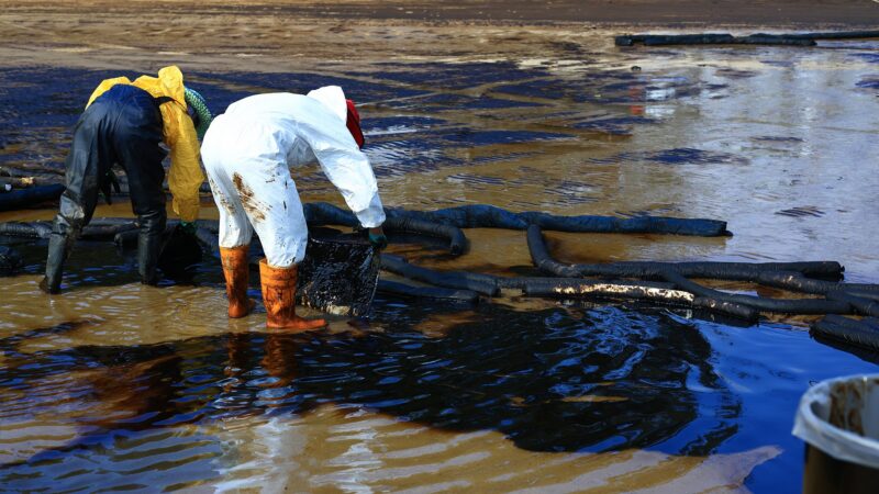 Professional team and volunteer wearing PPE clean up dirty of oil spill on the beach, oil slick washed up on a sand beach