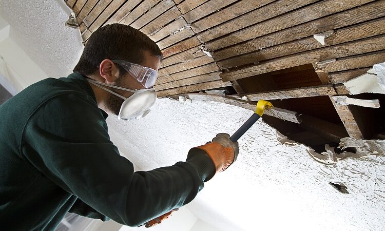man removing plaster lathe from ceiling with a crowbar